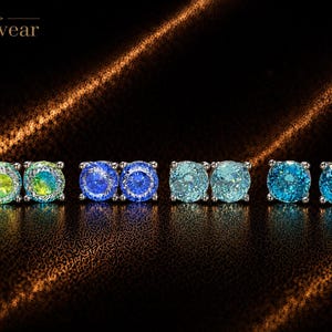 May include: Four pairs of round stud earrings with the brand name Monvear in the top left corner. The earrings feature faceted stones in varying colors: iridescent green and yellow, deep blue, light aqua, and bright turquoise, all set in silver.