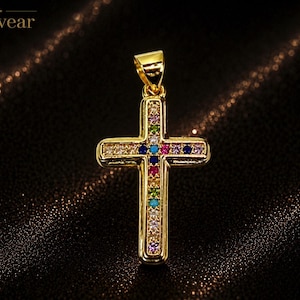 May include: A gold-toned cross pendant featuring a central row of multicolored gemstones, including blue, pink, green, and clear stones. The cross has a polished metallic finish and includes a bail at the top for attachment to a chain or necklace.