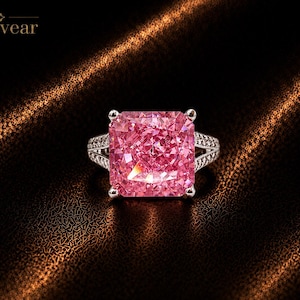 May include: A ring featuring a large, square-cut pink gemstone held by four silver prongs. The band is made of silver and is encrusted with small, clear stones along the sides. The text Monvear is visible in the upper left corner of the image.