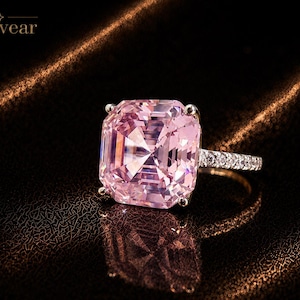 Op de afbeelding: Een ring met een grote, vierkant geslepen roze edelsteen in een zetting met vier pootjes, en een ringband bezet met kleine, heldere steentjes. De merknaam Monvear is zichtbaar in de linkerbovenhoek van de afbeelding.