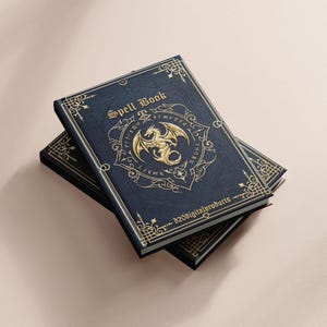 May include: Two spell books with a dark blue cover and gold detailing. The top book features the words "Spell Book" and a gold dragon emblem. The books are stacked on top of each other.