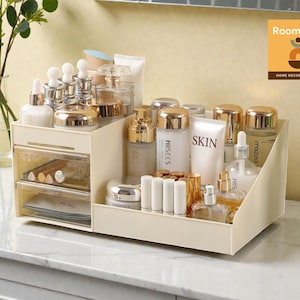 May include: A beige cosmetic organizer with multiple compartments and drawers, filled with various skincare products, including bottles, jars, and tubes. A clear glass vase with green stems is visible in the background.