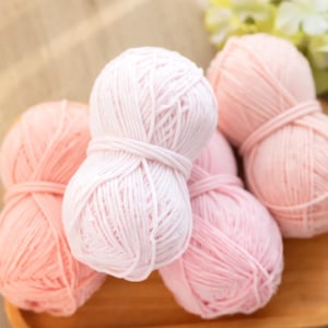 May include: A collection of light pink yarn balls, tightly wound and secured with yarn ties, are displayed on a wooden surface. The yarn's soft texture and pastel hue suggest a craft project. The scene evokes a sense of gentle creativity.