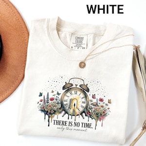 May include: Cream-coloured Comfort Colors t-shirt with a clock design and floral and butterfly details. The clock face has Roman numerals and the text "THERE IS NO TIME. only this moment." is printed below the clock.