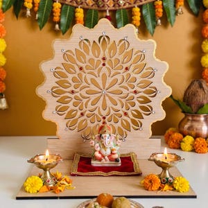 Op de afbeelding: Een houten altaar met een lasergesneden mandala-achtergrond met ingebedde kristallen, een klein Ganesha-beeldje op een rood fluwelen kussen, twee brandende koperen olielampen en een bord met snoepjes op een platte houten basis.