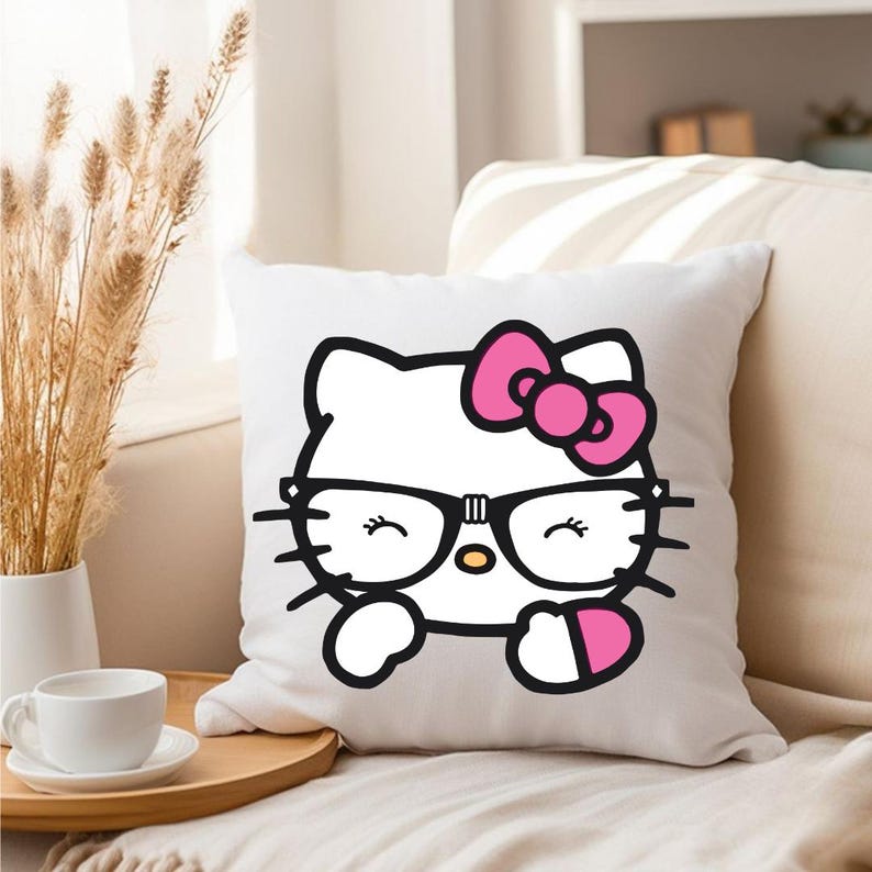 Puede incluir: Coj&iacute;n cuadrado blanco con una imagen de dibujos animados de Hello Kitty con gafas negras y un lazo rosa. El dise&ntilde;o tiene contornos negros y acentos rosas. El coj&iacute;n est&aacute; sobre un sof&aacute; claro.