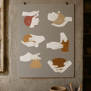 Puede incluir: Un grabado enmarcado que muestra ilustraciones de manos haciendo cerámica. El grabado está montado sobre un fondo gris. La imagen también muestra varios cuencos de cerámica y un jarrón sobre una mesa de madera, con una paleta de colores neutros.