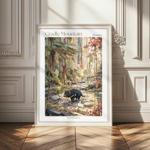 May include: A framed art print featuring a forest scene at Cradle Mountain, Tasmania, Australia. The illustration depicts a black Tasmanian devil standing near a rocky stream surrounded by tall trees, ferns, and foliage in shades of green and red.