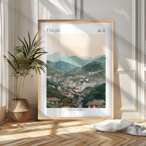 May include: A framed art print of Daegu, South Korea, featuring a watercolor-style depiction of a city nestled in a valley surrounded by mountains. The print includes the city's name in English and Korean.