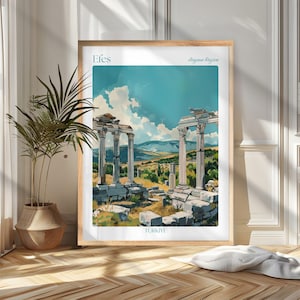 May include: A framed art print depicting ancient ruins with white columns under a blue sky. The print is labelled "Efes" and "Aegean Region" with "TURKIYE" at the bottom. The frame is light wood. The print is in a room with a plant.