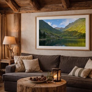 以下が含まれることがあります： 暗い灰色のソファの上に額入りの風景プリントがある居心地の良いリビングルーム。 部屋には木製のコーヒーテーブル、点灯したキャンドルランタン、窓から見える山の景色があります。