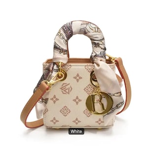 May include: White handbag with a patterned design and a decorative scarf tied to the handle. The bag has a gold-colored charm and a detachable tan strap. The word "White" is printed at the bottom of the image.