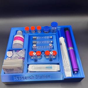 Puede incluir: Un organizador de estaci&oacute;n de investigaci&oacute;n de pl&aacute;stico azul con varios viales, jeringas y toallitas con alcohol. El organizador tiene compartimentos para diferentes art&iacute;culos, incluyendo un bol&iacute;grafo morado y botellas con tapas naranjas y azules. El texto "Research Station" es visible.