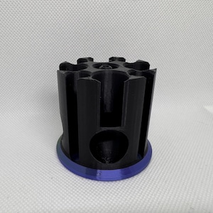 Puede incluir: Un objeto cil&iacute;ndrico negro con una serie de ranuras verticales y una base circular con un borde azul. La parte superior tiene un patr&oacute;n en forma de estrella. El objeto parece estar impreso en 3D.