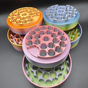 May include: A collection of colorful, 3D-printed storage containers. Each container is round with multiple circular holes on the top and a matching base. The colors include orange, pink, purple, blue, and green, with some containers displaying a rainbow gradient.