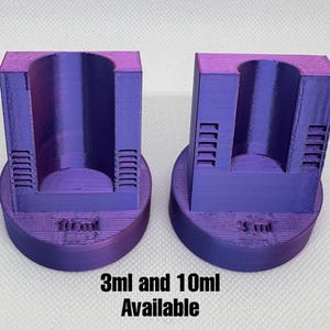 May include: Two purple 3D-printed measuring tools. One is labeled "10 ml" and the other "3 ml". The text "3ml and 10ml Available" is printed below the tools. Each tool has a cylindrical opening and a rectangular body with vertical slots.