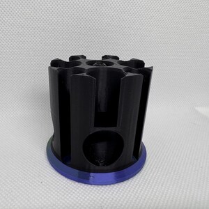 Puede incluir: Un objeto cil&iacute;ndrico negro con una base azul. La parte superior tiene m&uacute;ltiples aberturas y los lados ranuras verticales. El objeto parece estar impreso en 3D y probablemente sea un soporte o organizador.