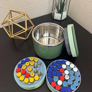 May include: An open, green insulated food container with a stainless steel interior sits next to two circular containers filled with small vials. The vials have colorful caps in red, yellow, blue, and white.