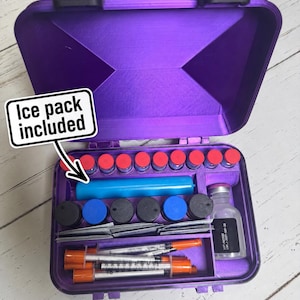 May include: A purple rectangular carrying case with a hinged lid containing a blue ice pack, multiple small vials with red and black caps, a larger glass vial, and several syringes with orange caps. The text "Ice pack included" is visible.