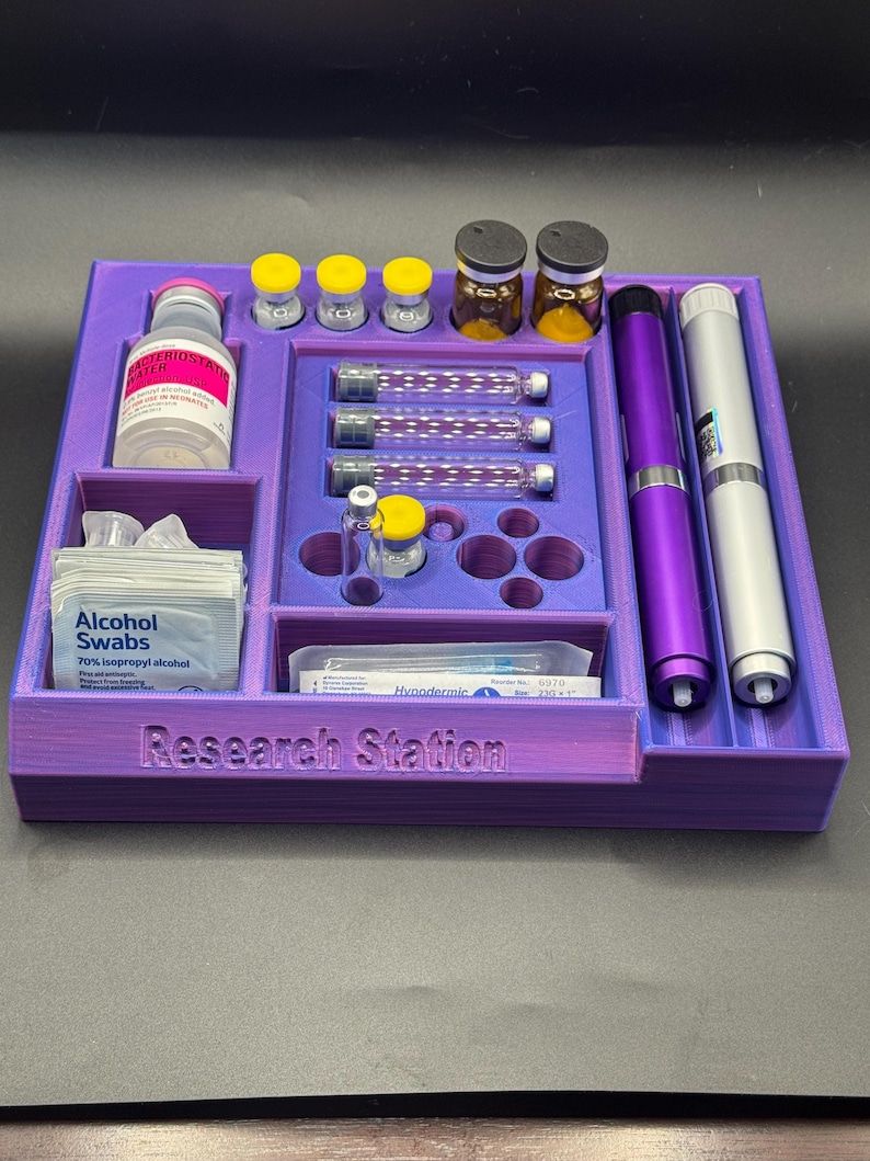 Puede incluir: Un organizador morado impreso en 3D, llamado "Research Station", que contiene viales, jeringas, toallitas con alcohol y dos bol&iacute;grafos. El organizador tiene m&uacute;ltiples compartimentos para diversos suministros m&eacute;dicos o de investigaci&oacute;n.
