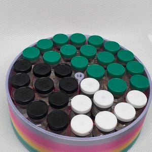 May include: A circular container with a rainbow-colored rim holds numerous small glass vials. The vials are capped with green, black, and white lids. The container is designed to hold and organize the vials.