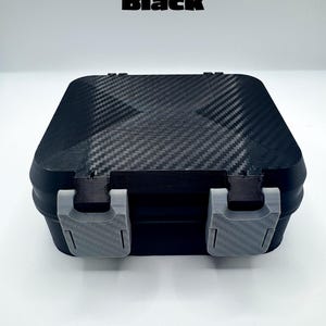 May include: A black rectangular storage box with a carbon fiber texture on the lid and two light gray plastic latches on the front. The word Black is printed in bold black letters above the box, which features a secure, closed design.