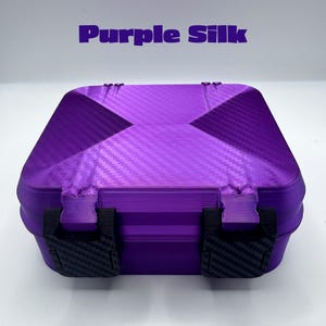 May include: A square purple storage box with a textured carbon fiber pattern on the lid and two black latches on the front. The text Purple Silk is printed in purple above the box. The container features a rigid construction with visible layers.