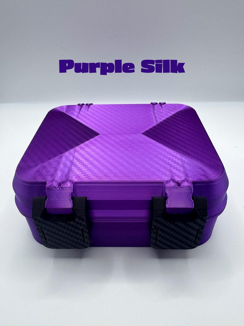 May include: A square purple storage box with a textured carbon fiber pattern on the lid and two black latches on the front. The text Purple Silk is printed in purple above the box. The container features a rigid construction with visible layers.