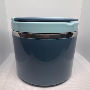 May include: A cylindrical, insulated food container in shades of blue and teal. The container has a stainless steel band and a matching lid. The design is sleek and modern, suitable for carrying lunches or snacks.