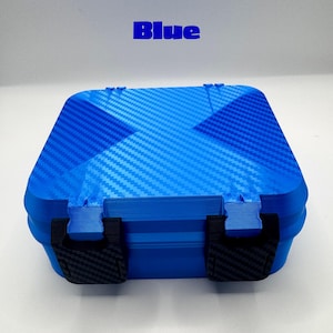 May include: A square blue storage case with a carbon fiber texture on the lid and two black latches on the front. The word Blue is printed in blue text above the case. The case features a hinged design and a textured finish on the lid surface.