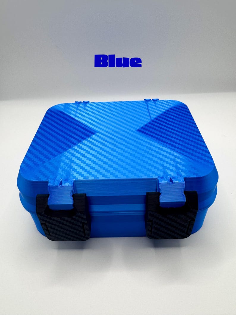 May include: A square blue storage case with a carbon fiber texture on the lid and two black latches on the front. The word Blue is printed in blue text above the case. The case features a hinged design and a textured finish on the lid surface.