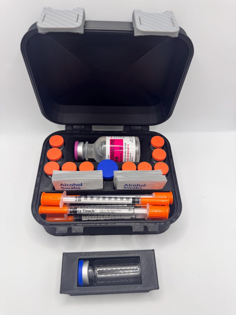 May include: A black carrying case containing medical supplies including a glass vial with a pink label, multiple small orange-capped vials, two stacks of alcohol swabs, and three Easy-Touch syringes with orange caps. A separate black holder holds one blue-capped vial.