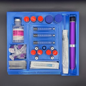 Puede incluir: Una bandeja azul con varios suministros m&eacute;dicos. Incluye una botella etiquetada como "Agua Bacteriost&aacute;tica", jeringas, agujas y viales con tapas rojas y azules. Tambi&eacute;n hay un dispositivo morado en forma de bol&iacute;grafo.