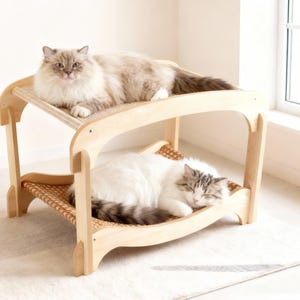 May include: A two-tiered cat bed made of light-coloured wood. Two cats are resting on the bed. The top level has a cat with light brown and grey fur. The bottom level has a white cat with grey markings.