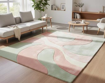 May include: A large, rectangular area rug with an abstract design in shades of pink, green, and white. The rug is placed on a hardwood floor in a living room setting, with a sofa and coffee table visible.