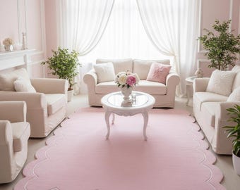May include: A light pink scalloped rug with a white border dominates a living room scene. The room features white sofas, armchairs, and a coffee table, all set against a backdrop of pink walls and white curtains. Decorative plants and flowers add to the room's aesthetic.
