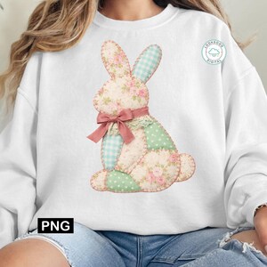 May include: White sweatshirt featuring a patchwork bunny design. The bunny has floral, gingham, and polka dot patterns in pastel colors, with a pink bow and lace collar. The design is a whimsical, springtime theme.