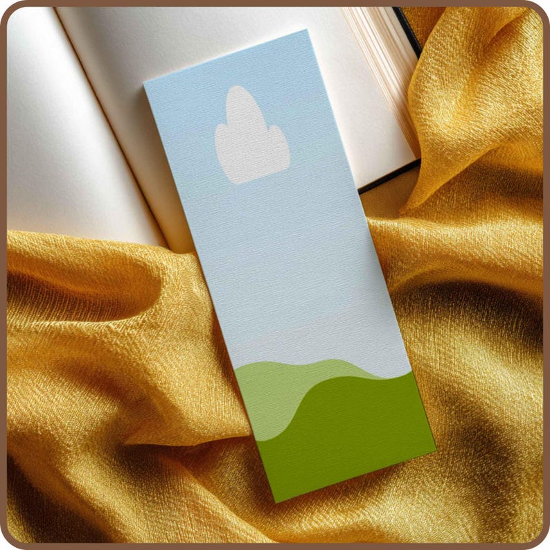 May include: A rectangular bookmark with a light blue sky design and a white cloud. The bottom of the bookmark features green rolling hills. The bookmark is resting on an open book and a gold fabric.