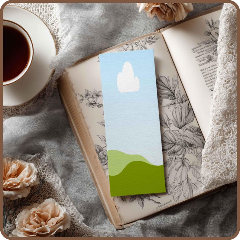 May include: A bookmark with a minimalist design featuring a blue sky, a white cloud, and green rolling hills. The bookmark is set against an open antique book with floral illustrations, a cup of tea, and flowers.