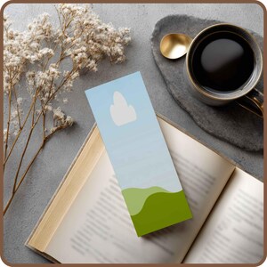 May include: A blue and green bookmark with a cloud design is placed in an open book. A cup of coffee and a gold spoon rest on a gray stone coaster. Dried flowers are in the background.