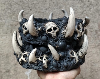 May include: A dark gray, skull-themed planter with large, off-white tusks and small skull details. The planter has a textured surface and a menacing appearance, suitable for Halloween or gothic decor.