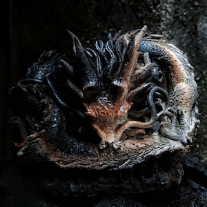 Puede incluir: Una escultura detallada de un dragón, con una superficie texturizada en marrón oscuro, negro y beige. La cabeza y el cuerpo del dragón están intrincadamente diseñados, con escamas y cuernos visibles. La escultura está sobre un fondo oscuro.