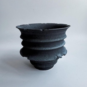 Vaso artesanal texturizado em preto e cinza para suculentas, com formato espiral e nervuras, em cerâmica rústica com acabamento lascado.
