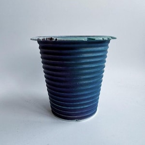 Op de afbeelding: Een handgemaakte keramische vaas met een geribbeld ontwerp. De vaas heeft een diepblauwe kleur met een licht gestructureerd oppervlak. De rand van de vaas heeft een lichtgroene tint. Een uniek decoratiestuk.