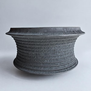 Puede incluir: Un cuenco de color gris carbón oscuro con un borde ancho y acampanado y un cuerpo cilíndrico. La superficie exterior presenta una textura estriada vertical fina y distintiva que envuelve toda la circunferencia del recipiente.