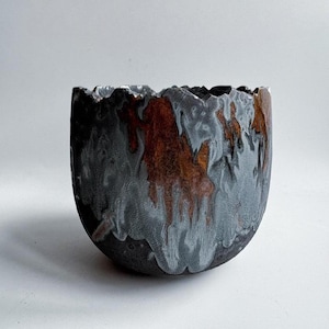 Peut inclure: Un bol en céramique fait à la main avec une surface texturée unique. Le bol présente une base sombre avec des accents gris et rouille, créant un contraste saisissant. Le bord a un bord irrégulier et dentelé, ajoutant à son attrait artistique.