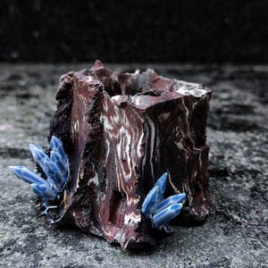 Puede incluir: Una maceta de cerámica cuadrada hecha a mano, con un aspecto rústico veteado en tonos marrón y blanco. Adornada con grupos de acentos azules en forma de cristal. La maceta está diseñada para plantas pequeñas o suculentas.