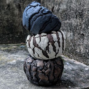 Peut inclure: Trois objets sphériques texturés empilés. La sphère supérieure est bleu foncé, celle du milieu est blanche avec des fissures marron et celle du bas est marron avec des fissures marron foncé. Les objets sont sur une surface grise.