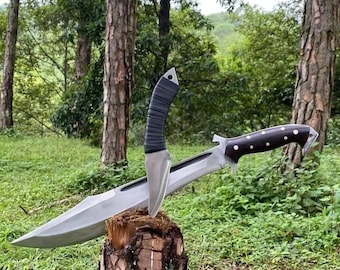 May include: Two knives are displayed on a tree stump. One knife has a silver blade and a black handle. The other knife has a silver blade and a dark brown handle with white dots. The knives are in a forest setting.