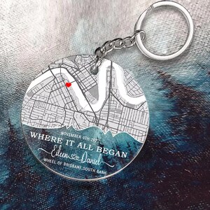 May include: A clear, circular keyring with a map design and a red heart marking a location. The text "WHERE IT ALL BEGAN" and names "Eileen & Daniel" are displayed, along with the date "NOVEMBER 9TH 2022" and "WHEEL OF BRISBANE, SOUTH BANK".